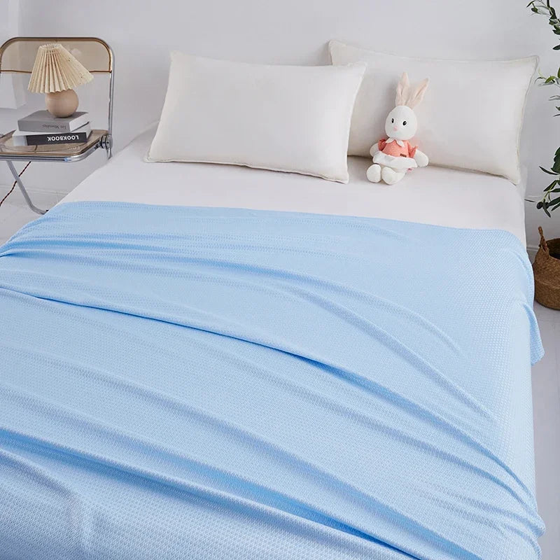 Une couverture de lit bleu clair reposant sur un lit blanc, avec des oreillers blancs et un jouet lapin blanc posé à côté.