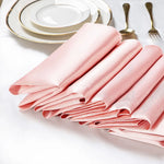 Serviettes en tissu rose élégantes et pliées avec des assiettes et des couverts dorés sur fond clair.