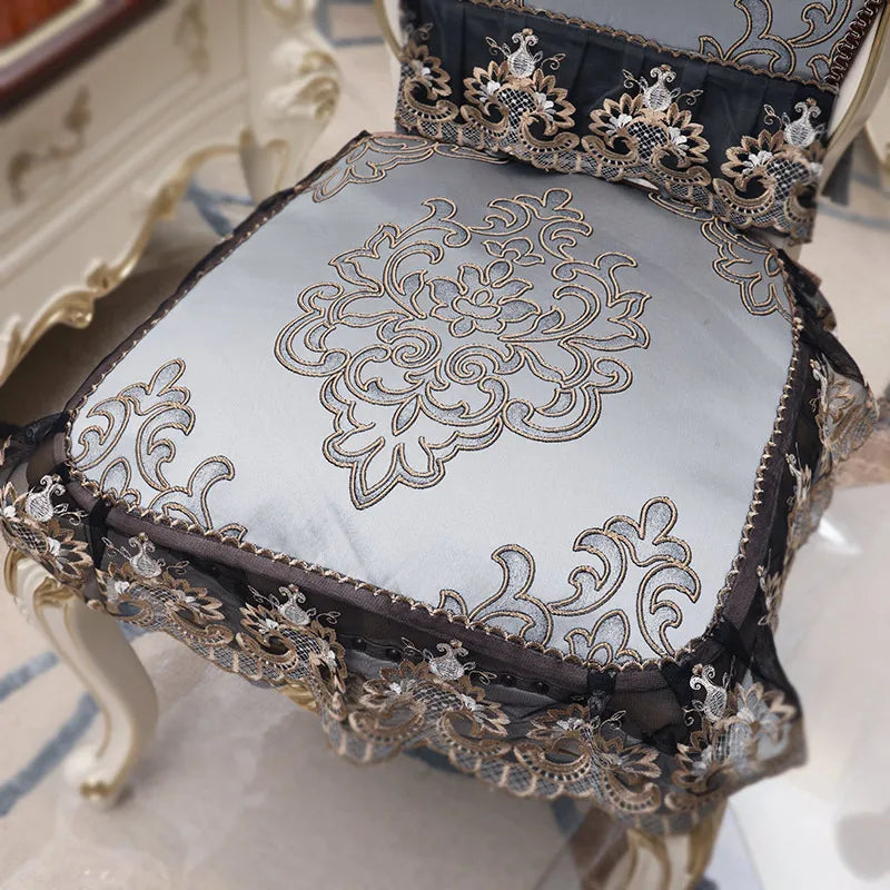 Coussin décoratif élégant avec des motifs floraux brodés et des bordures ornementales en couleurs neutres.