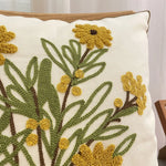 Coussin décoré de jolies fleurs jaunes et vertes brodées avec soin sur un fond blanc.