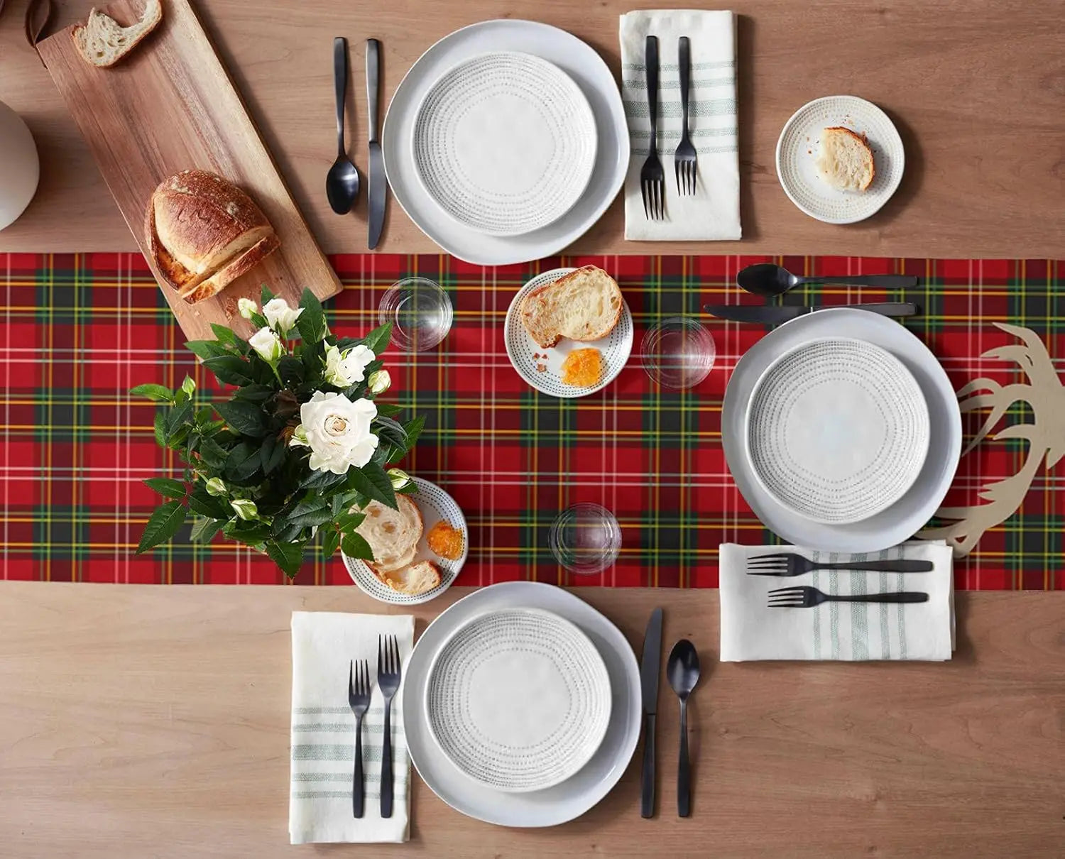 Table dressée avec des plats et des ustensiles sur un napperon à carreaux rouges, accompagnée d'un bouquet de fleurs blanches.