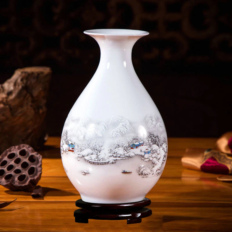 Un vase en porcelaine blanche orné d'une scène hivernale peinte, avec des maisons dans un paysage enneigé, sur un support en bois.