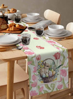 Table de petit-déjeuner élégante avec une nappe ornée de fleurs de tulipes roses et d'un panier de Pâques contenant un lapin mignon, accompagnée de plats et de couverts.