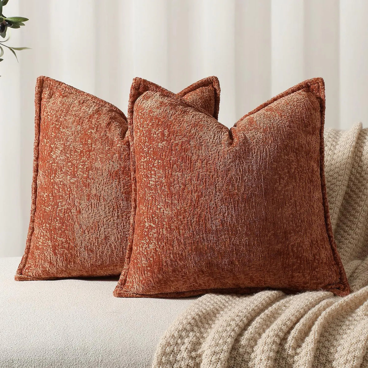 Ensemble de coussins décoratifs en textile brun rougeâtre aux textures luxueuses, sur fond de couverture beige moelleuse.
