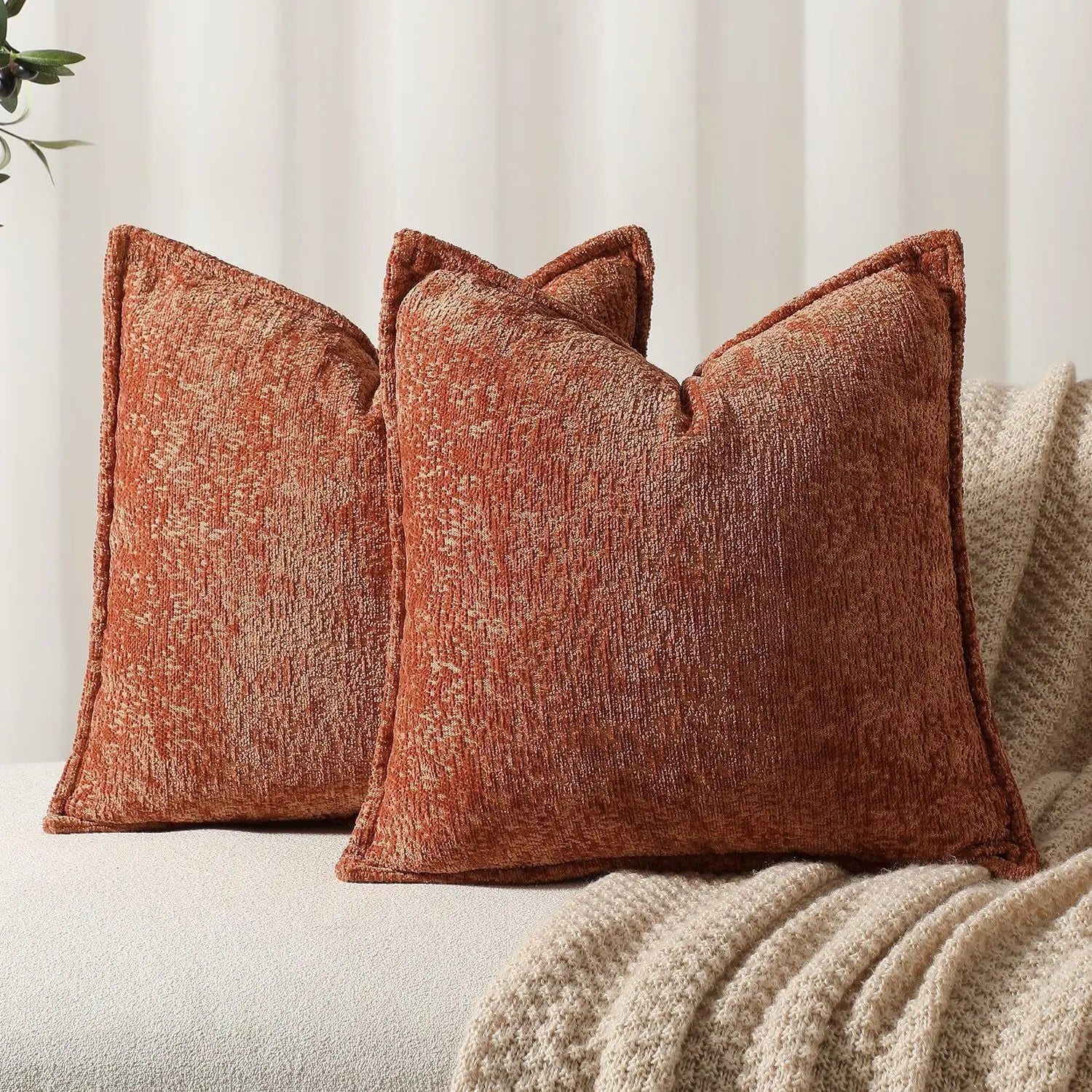 Ensemble de coussins décoratifs en textile brun rougeâtre aux textures luxueuses, sur fond de couverture beige moelleuse.