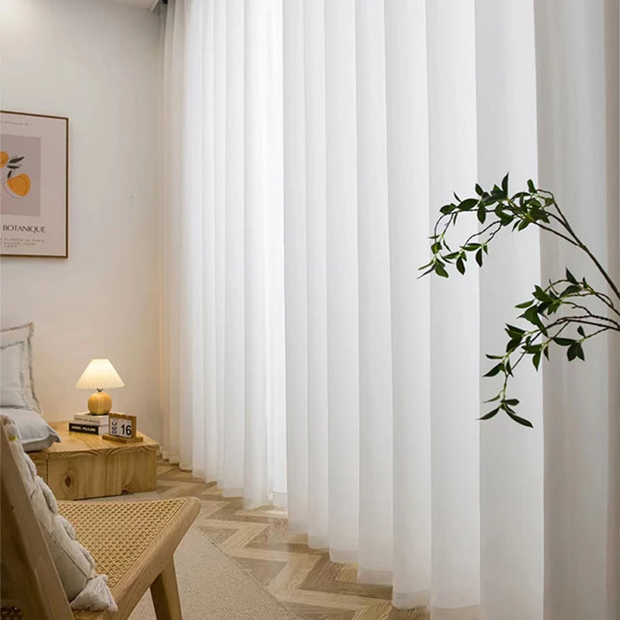 Voilage blanc translucide installé dans un salon minimaliste avec fauteuil en rotin, table basse en bois clair et cadre décoratif mural.