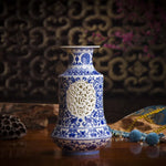 Vase en porcelaine bleue et blanche orné de motifs floraux et géométriques élégants, posé sur une surface en bois avec des accessoires décoratifs.