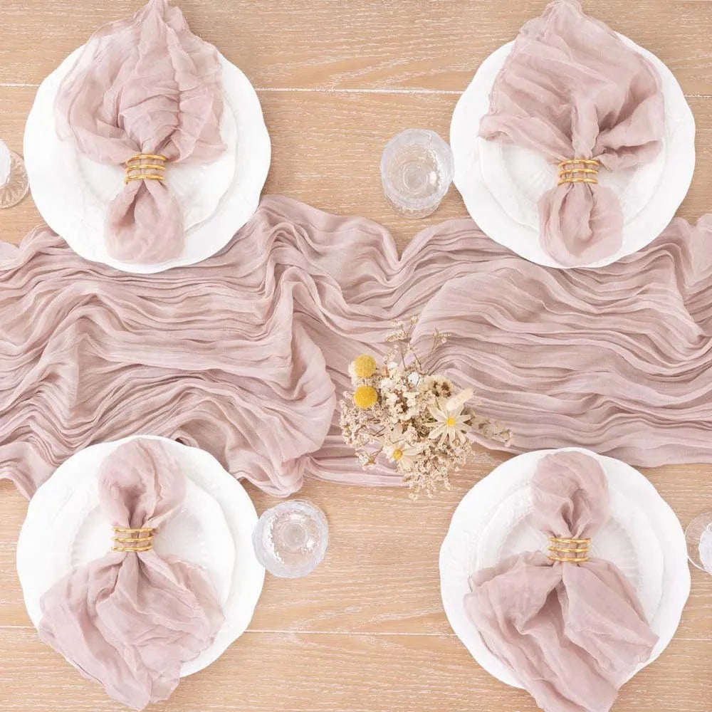 Élégants plis de tissu rose pâle sur une table en bois clair, avec des fleurs sauvages au centre, créant une atmosphère douce et raffinée.