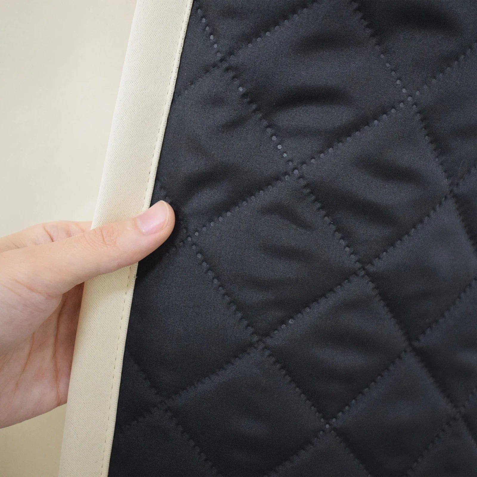 Gros plan d'une main tenant un produit avec un motif matelassé noir et des bordures claires. Le design en losanges géométriques évoque une finition élégante et moderne, idéal pour une décoration intérieure sophistiquée. L'image met en valeur la qualité et le souci du détail.