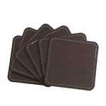 Des sets de sous-verres carrés en cuir marron foncé avec une couture blanche, offrant une finition élégante et durable.