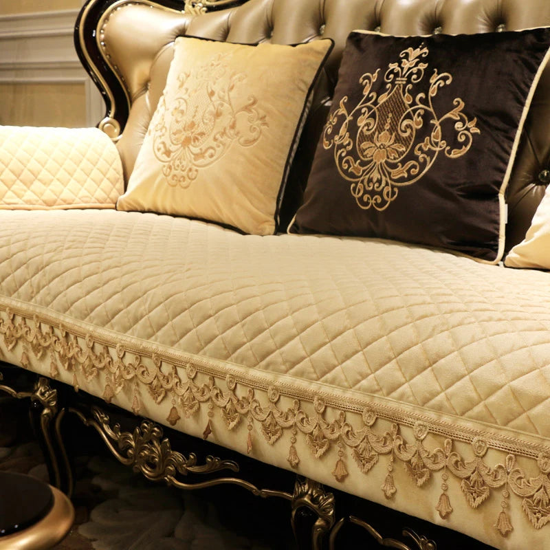 Une élégante collection de coussins et d'une courtepointe matelassée sur un canapé de style baroque ornementé avec des motifs floraux dorés.