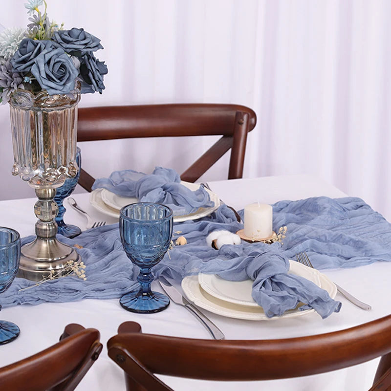 Une magnifique table dressée avec des fleurs bleues, des photophores et de la vaisselle élégante sur un fond blanc.