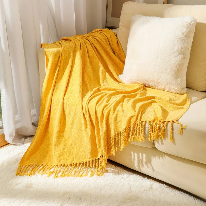 Une couverture moelleuse et frangée en couleur jaune moutarde posée sur un canapé blanc et beige.