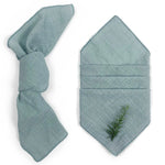 Serviette pliée verte pâle avec un ornement de branche de conifère, suggérant une ambiance apaisante et naturelle.