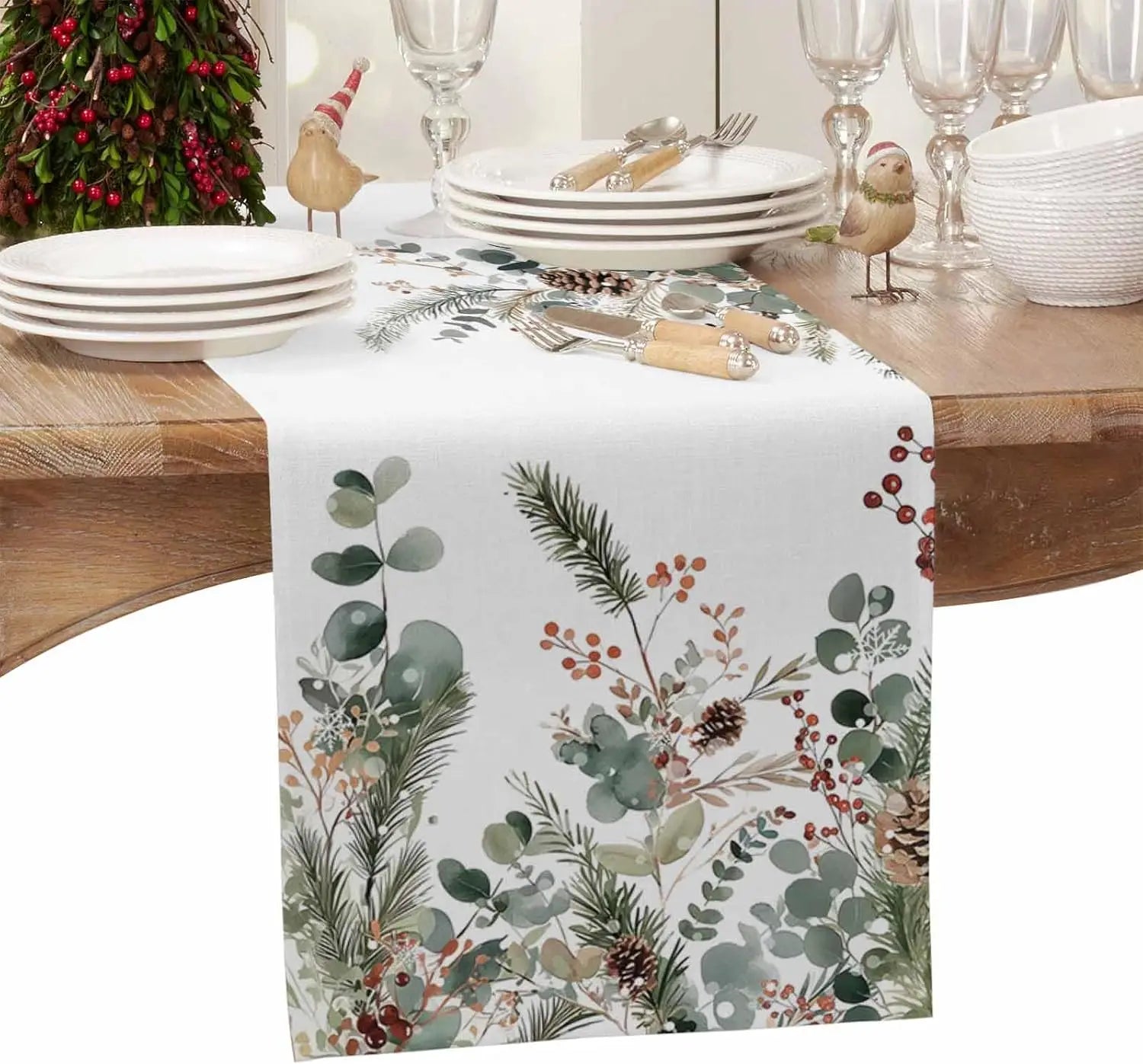 Table dressée pour Noël avec une belle nappe ornée de motifs de branches d'arbres, de baies rouges et de figurines d'oiseaux.