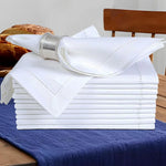 Pile de serviettes de table blanches sur une nappe bleue, avec un beau bracelet argenté et des viennoiseries sur le côté.