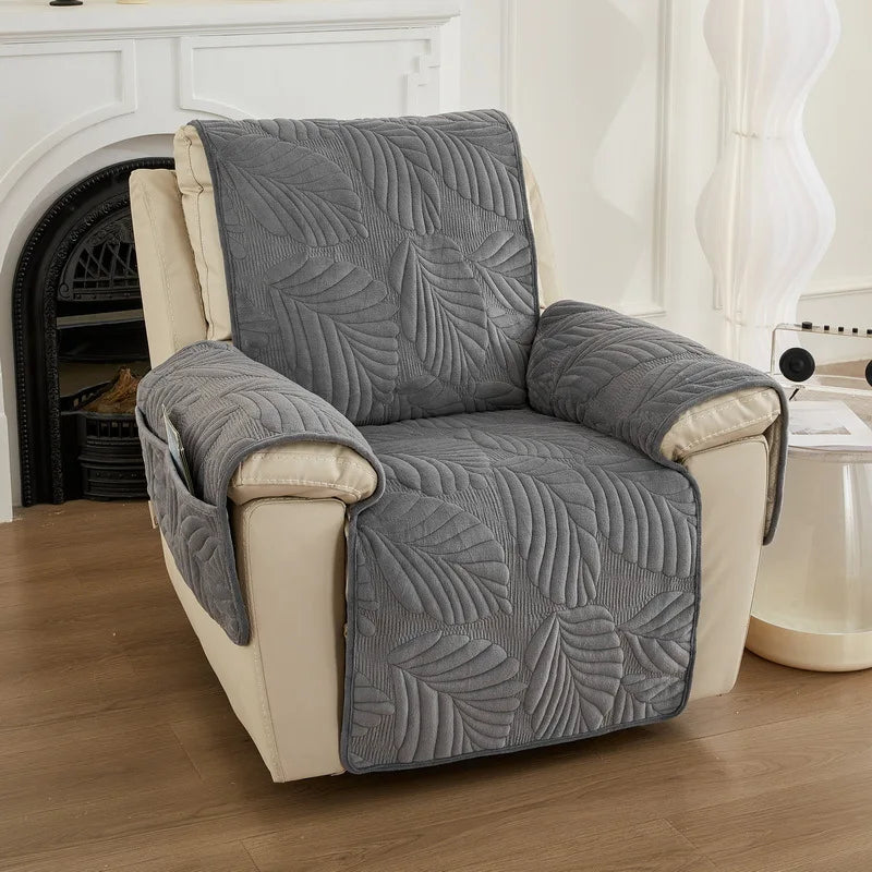 Un fauteuil confortable recouvert d'un motif de feuilles gris, placé dans un salon lumineux avec une cheminée.