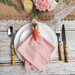 Une table de dîner élégante avec des fleurs, des bougies et des couverts dorés sur une nappe en lin rose.