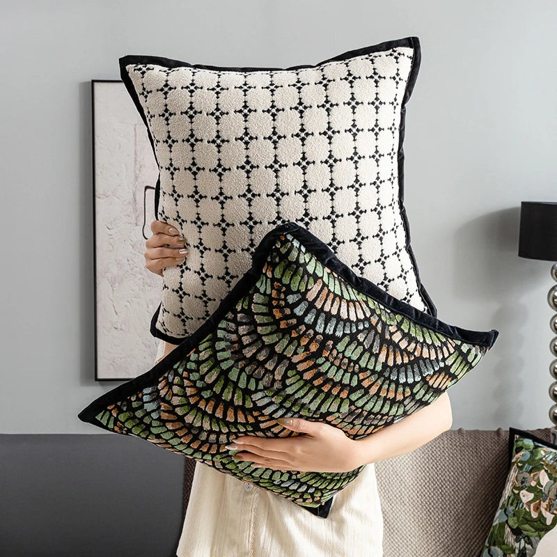 Coussin décoratif noir et blanc orné de motifs géométriques élégants, avec un coussin de sofa multicolore et vibrant placé devant.