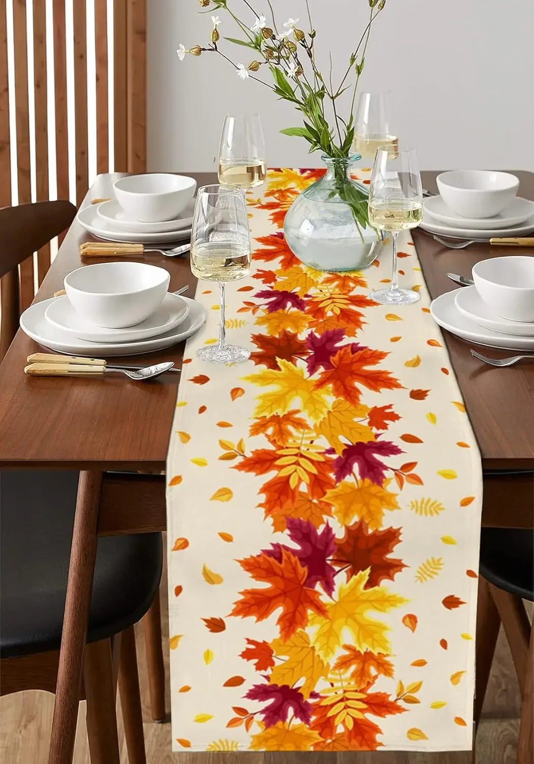 Élégante table de salle à manger avec service de vaisselle blanche, verres de vin et bouquet de fleurs sauvages, décorée d'un chemin de table automnale représentant de magnifiques feuilles d'érable colorées.