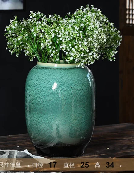 Un magnifique bouquet de petites fleurs blanches dans un vase en céramique vert brillant, posé sur un bureau en bois sombre.