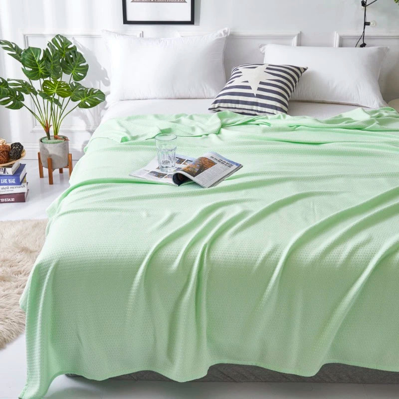 Une chambre à coucher confortable avec des draps et des oreillers blancs, une couverture verte pomme, et un bel arrangement de plantes à côté du lit.