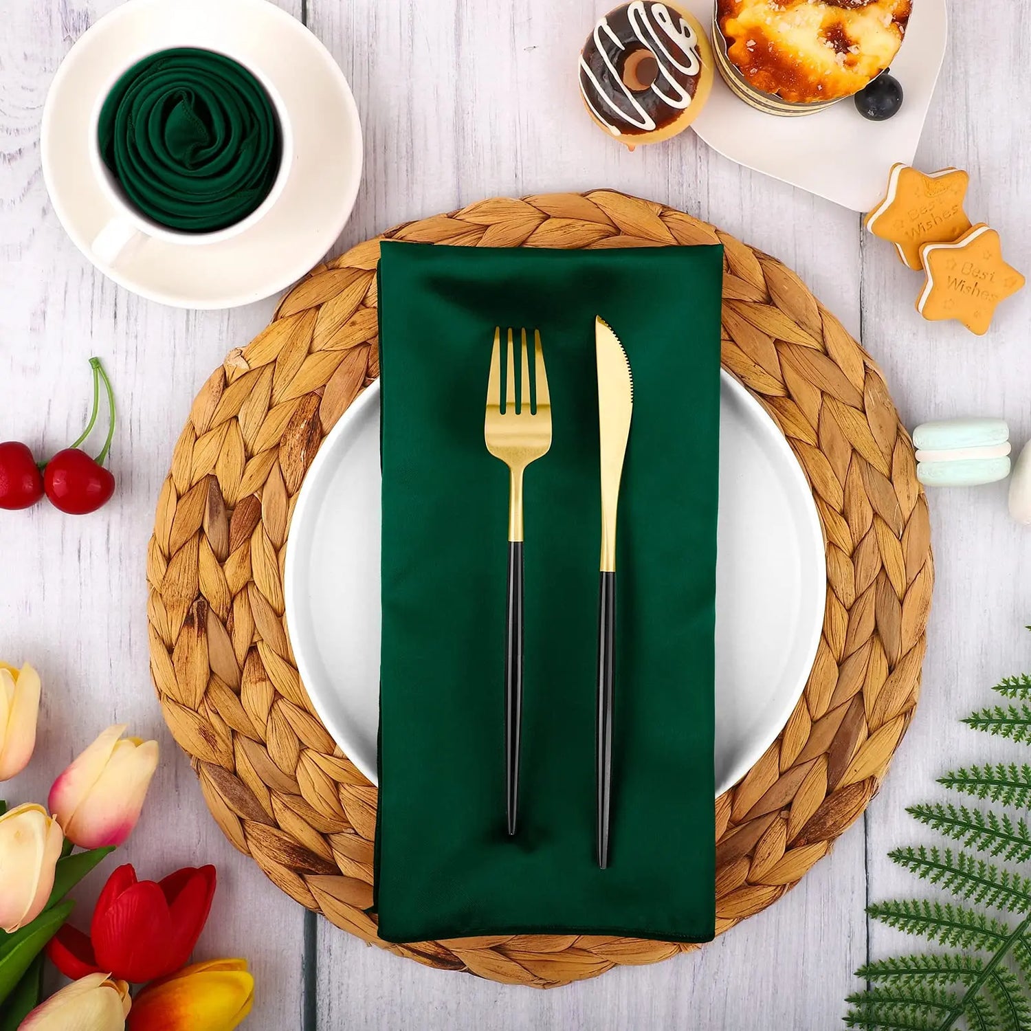 Une table de décoration élégante avec une assiette, des couverts dorés sur une serviette verte, entourée de fleurs et de gâteaux.