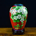 Un vase décoratif émaillé de motifs floraux colorés et exotiques sur un fond rouge vif, créant une pièce unique et captivante.