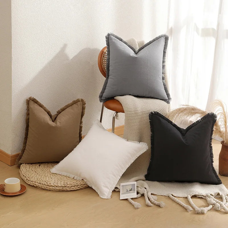 Assortiment de coussins décoratifs en tons neutres avec des détails texturés, disposés sur un plancher en bois clair avec une bougie allumée.