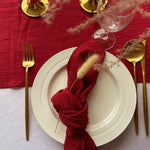 Une table de fête chic avec un service en argent et une serviette de table rouge enroulée avec un ornement décoratif.