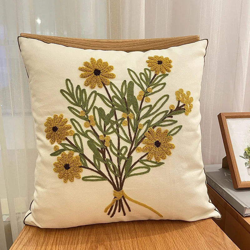 Coussin décoratif avec un joli bouquet de fleurs dorées et vertes sur un fond beige.