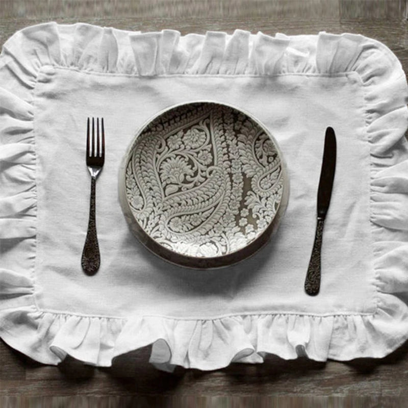Une assiette en porcelaine décorée d'un motif floral élégant, entourée d'une nappe blanche à volants, avec une fourchette et un couteau sophistiqués.