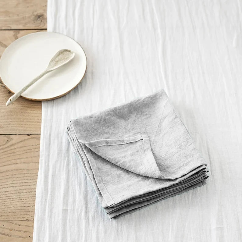 Un jeu de serviettes grises en lin posé sur une surface en bois avec un bol blanc.