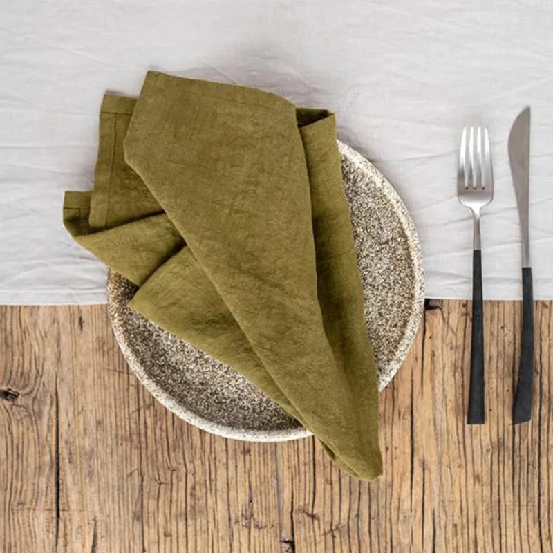 Des serviettes de table en lin vert et une assiette en pierre posées sur une table en bois rustique, avec des couverts en métal.