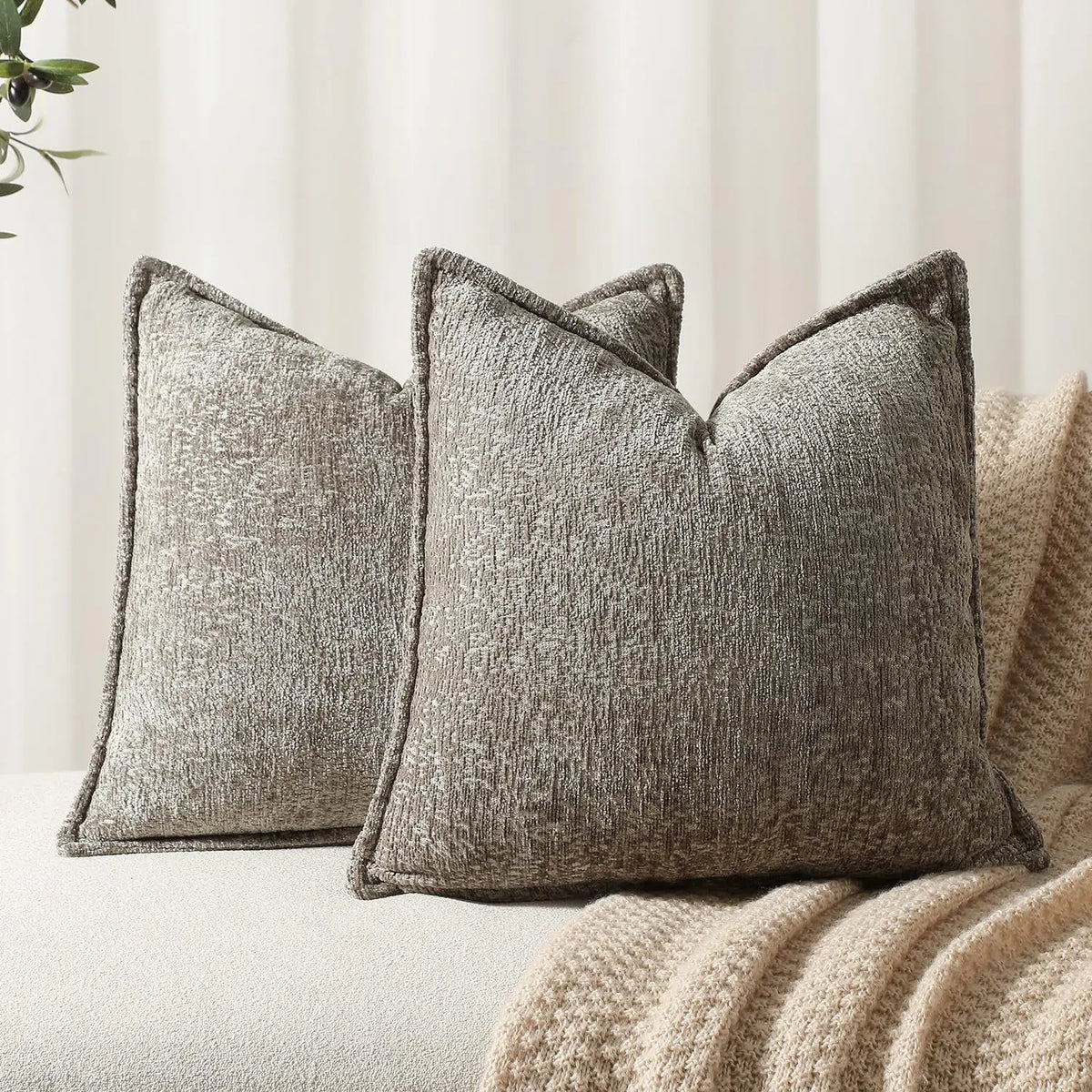 Trois élégants coussins gris en velours texturé, disposés de manière harmonieuse sur un canapé blanc.