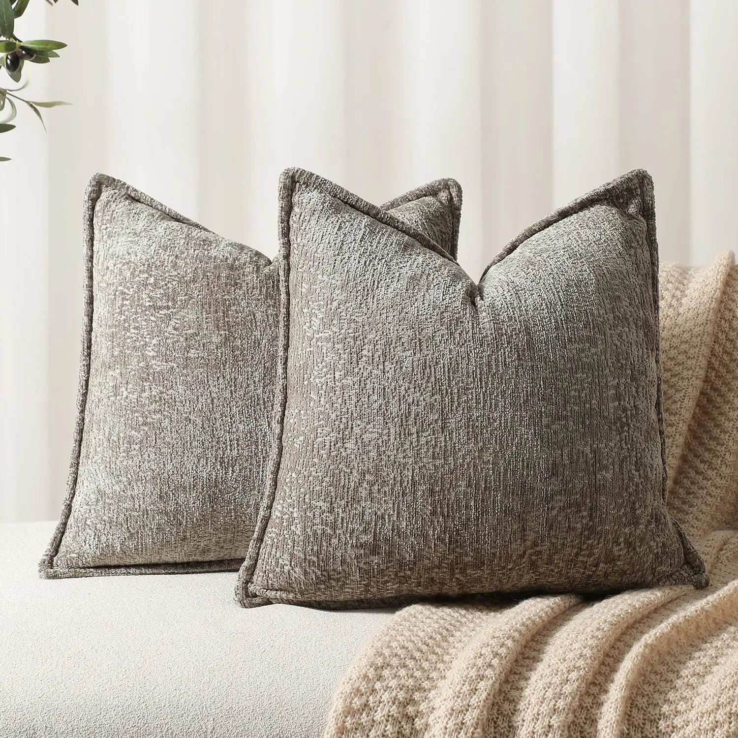 Trois élégants coussins gris en velours texturé, disposés de manière harmonieuse sur un canapé blanc.