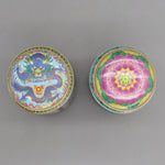 Deux boîtes colorées ornées de motifs traditionnels orientaux, l'une montrant un dragon bleu enroulé, l'autre une fleur rose épanouie, représentant une riche tradition décorative.