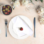 Une assiette blanche avec une fraise mûre posée délicatement, entourée de fleurs de pivoines blanches, de fruits rouges dans un bol et de couverts sur un fond neutre et élégant.