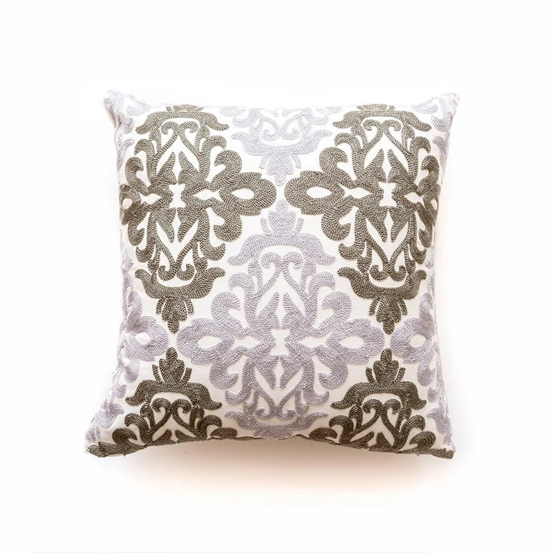 Oreiller décoratif avec motif de fleurs et de feuilles en broderie blanche et taupe sur un fond blanc.
