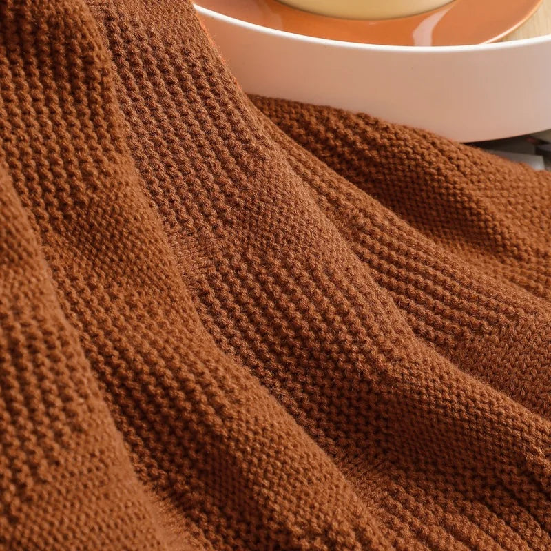 Un plaid en tricot de laine d'un riche ton de rouille, avec un motif de points et de rayures, donnant une impression douce et confortable.