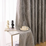 Rideau élégant avec motif ondulé en gris, suspendu près d'une table en verre moderne. Accessoirisée avec des bougeoirs décoratifs et une tasse à café, cette mise en scène ajoute une touche sophistiquée et contemporaine à tout intérieur. Idéal pour embellir le salon ou la chambre à coucher.