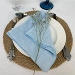 Une table élégamment dressée avec des accessoires en verre, des couverts en argent et une serviette en lin bleu ciel accentuée par une touche florale délicate.