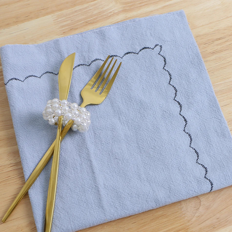 Une serviette de table grise avec une fourchette et un couteau dorés ornés de perles élégantes.