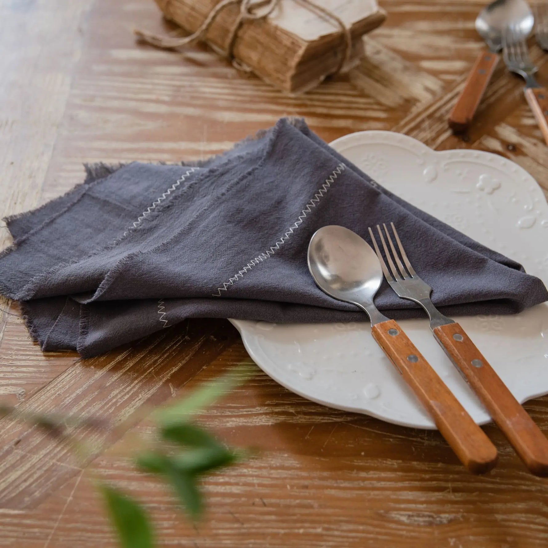L'image montre un arrangement de table avec des couverts en acier inoxydable et un linge de table gris sur un fond en bois, suggérant un cadre rustique et naturel pour un repas.