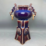Cette impressionnante pièce de céramique ornée de motifs dorés et bleu foncé présente un vase central élégamment ouvragé.