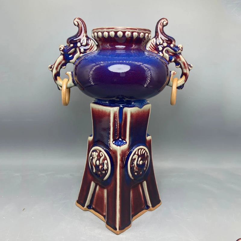 Cette impressionnante pièce de céramique ornée de motifs dorés et bleu foncé présente un vase central élégamment ouvragé.
