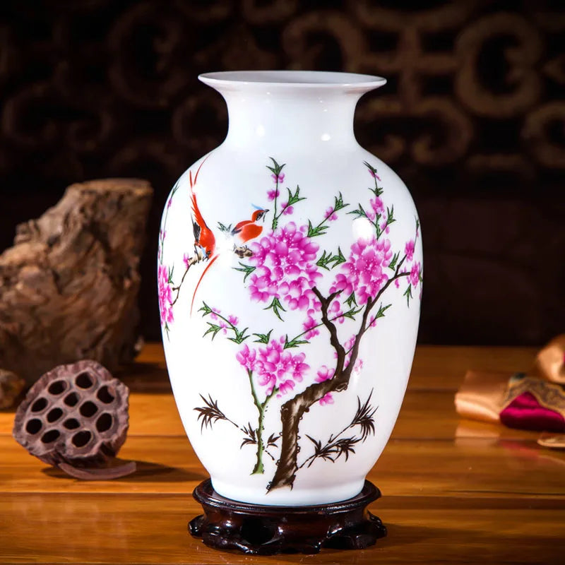 Une élégante poterie blanche ornée de fleurs de pivoines roses et de petits oiseaux rouges, sur un socle en bois sombre, dégageant une atmosphère traditionnelle et raffinée.