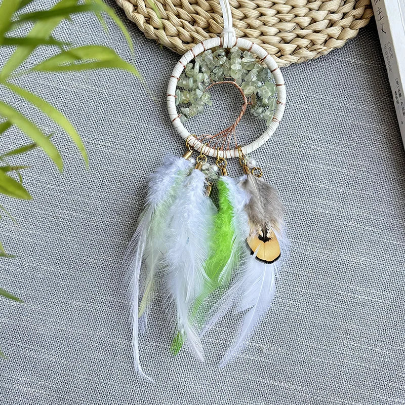 Capteur de rêves naturel avec anneaux en fil tressé, pierres décoratives et plumes blanches et vertes, sur un fond de feuilles et de texture tressée.