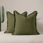 Des oreillers décoratifs de couleur verte foncée avec des franges texturées sur les bords, offrant un style bohème élégant.