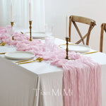 Une table élégante décorée de bougies, de vaisselle blanche et de tissus rose pâle drapés avec style, créant une ambiance sophistiquée et féminine.